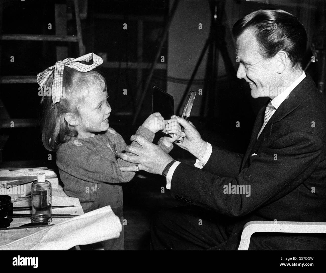 JOHN AND HAYLEY MILLS 1951: Grease paint is as familiar as picture books to Hayley Mills (5), seen giving her father, actor John Mills, a helping hand with his make-up on set at Shepperton studios where he is starring in 'Mr Dunning Drives North'. Stock Photo