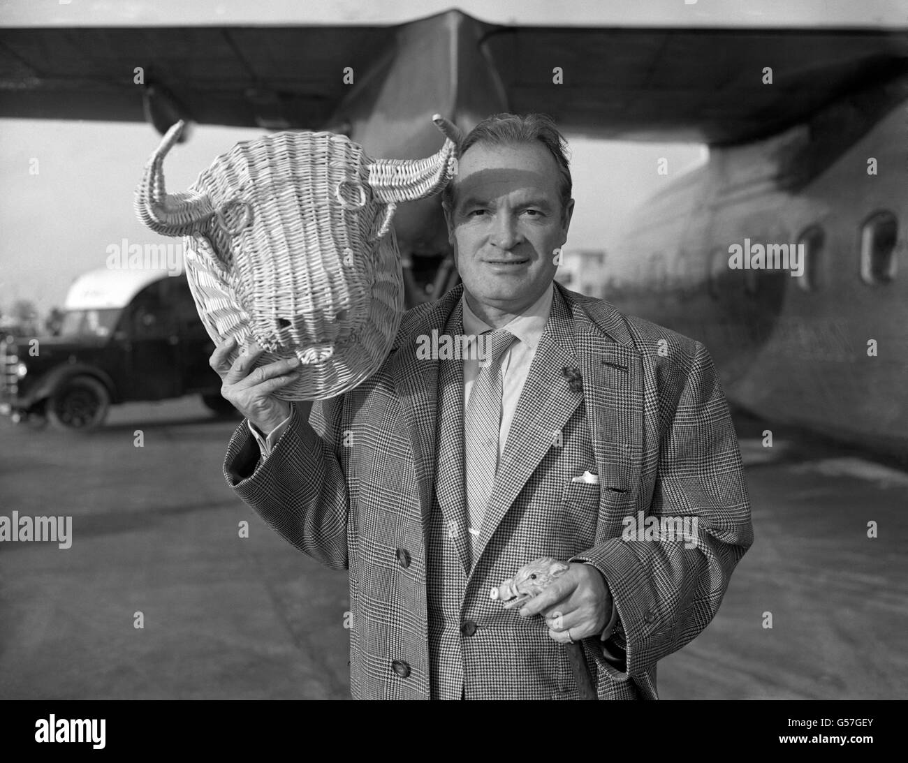 American entertainer Bob Hope hopping back from across Europe after a flying visit to Madrid pictured at London Airport with a souvenir, called 'Crosby', from Spain. Stock Photo