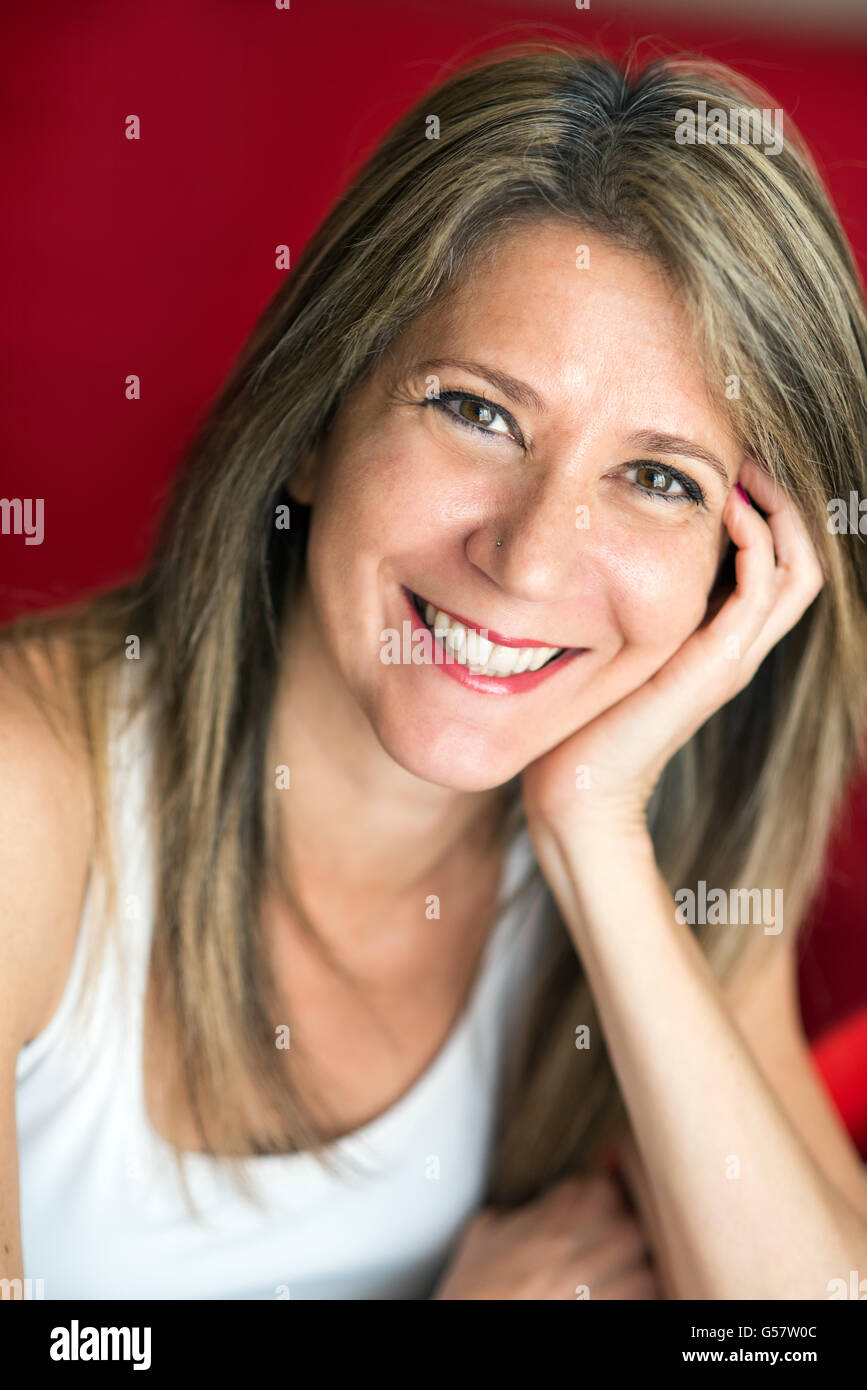 Close up Attractive Adult Woman Leaning her Face on her Hand and Smiling at the Camera Against Red Background. Stock Photo