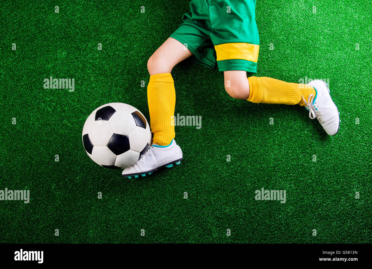 Unrecognizable little football player against green grass, studi Stock