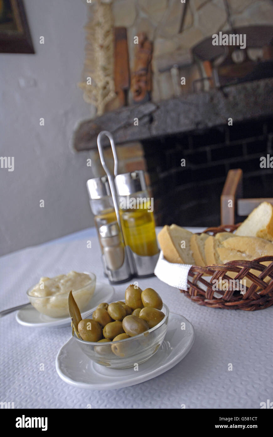 Table with alioli, spanish green olives, bread and oil, salt, pepper and vinegar, with a rural chimney behind Stock Photo