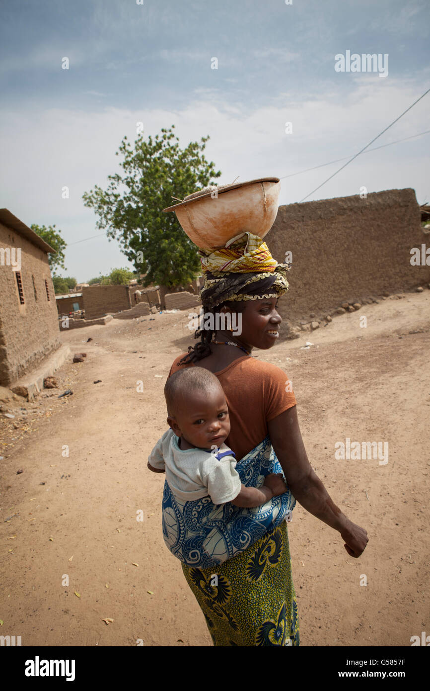 A woman carries a child on her back in Niassan village, Burkina Faso. Stock Photo