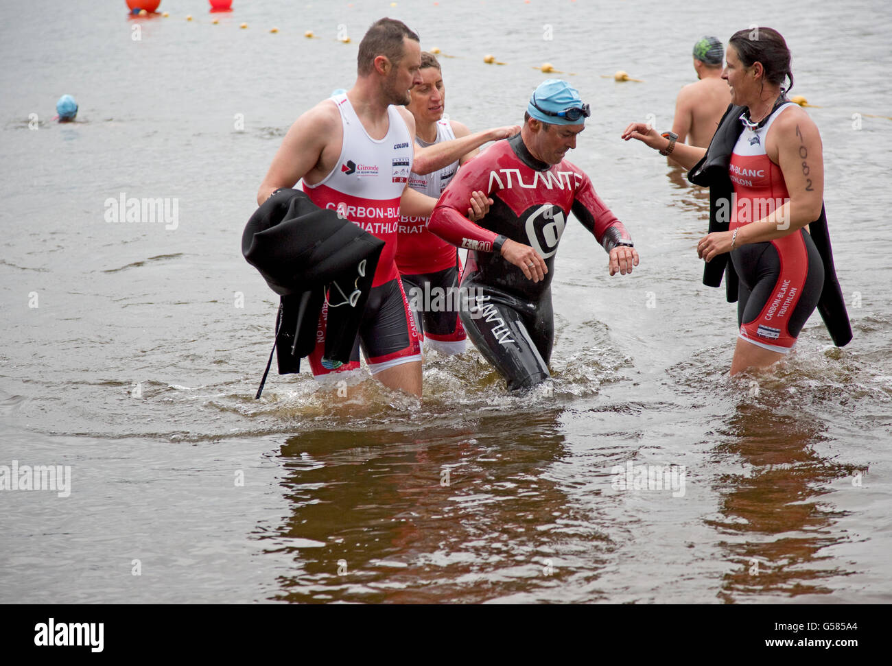 Swimmers helping teammate out of water at end lake swim Triathlon Mimizam France Stock Photo