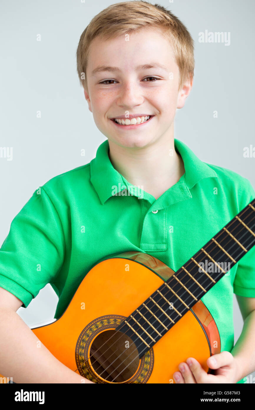 Portrait of a young boy posing for the camera with a guitar. He is standing in front of a plain background Stock Photo