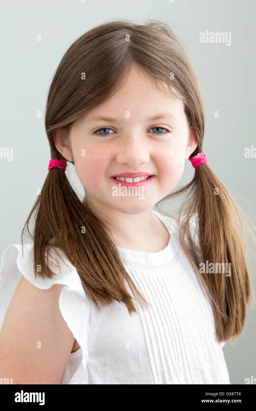 Portrait of a young girl. She has her hair in pigtails and is smiling at the camera against a plain blackground Stock Photo