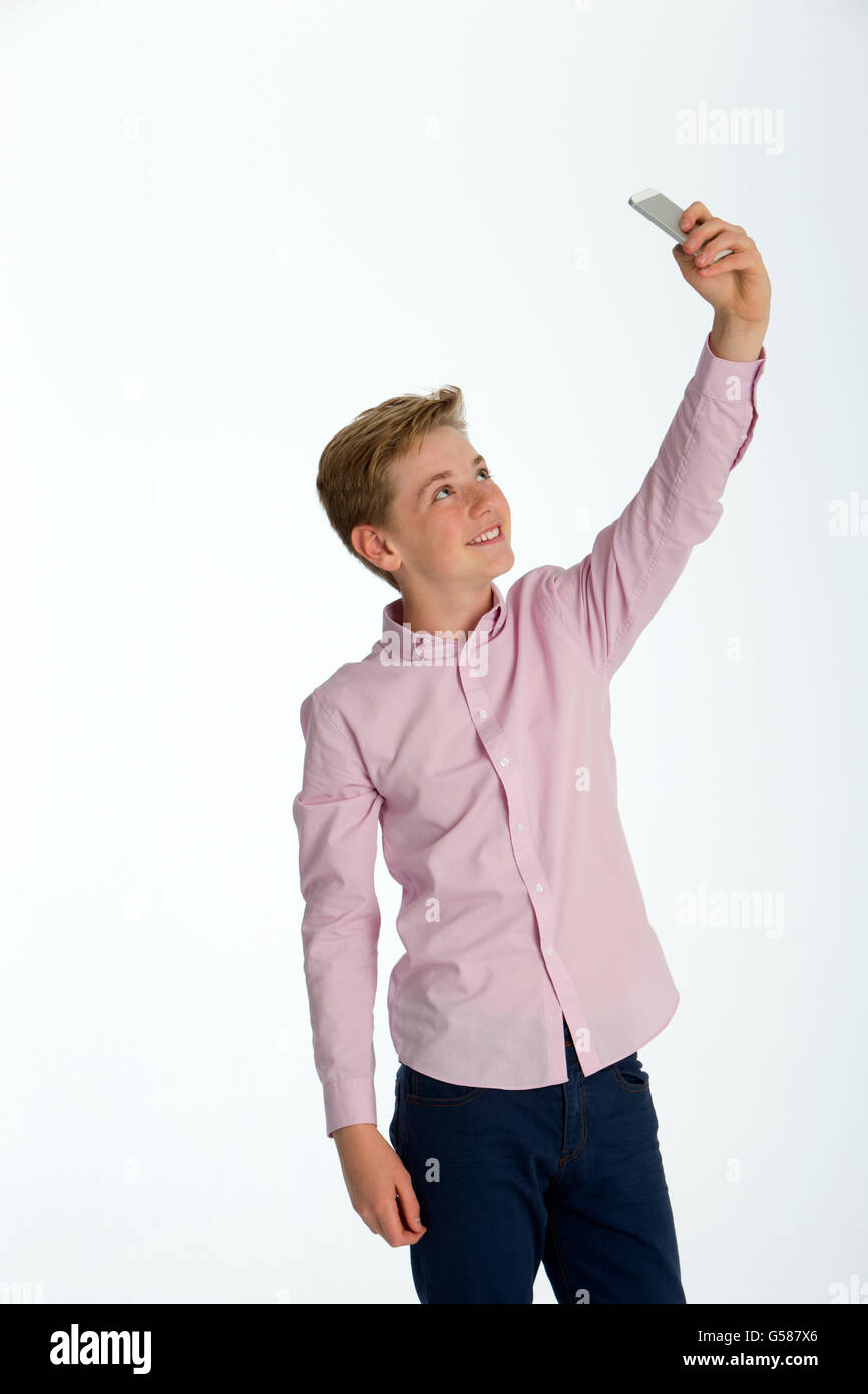 Young boy taking a selfie on a smartphone against a white background Stock Photo