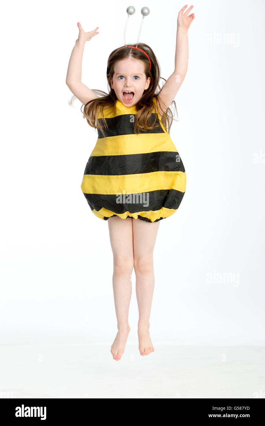 Little girl in a bumble bee costume posing in midair against a white background Stock Photo