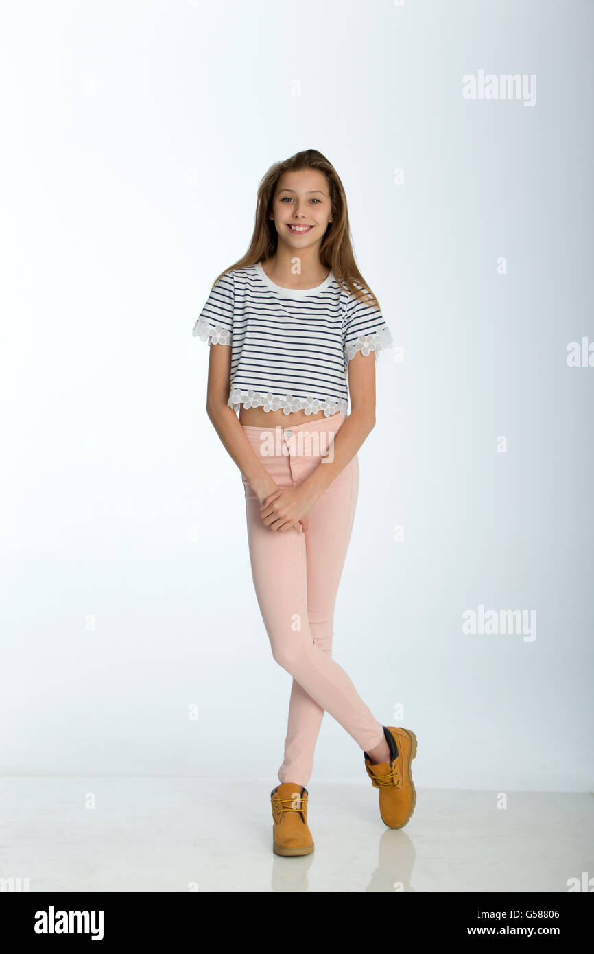 Full length portrait of a young girl against a white background. She is smiling for the camera. Stock Photo