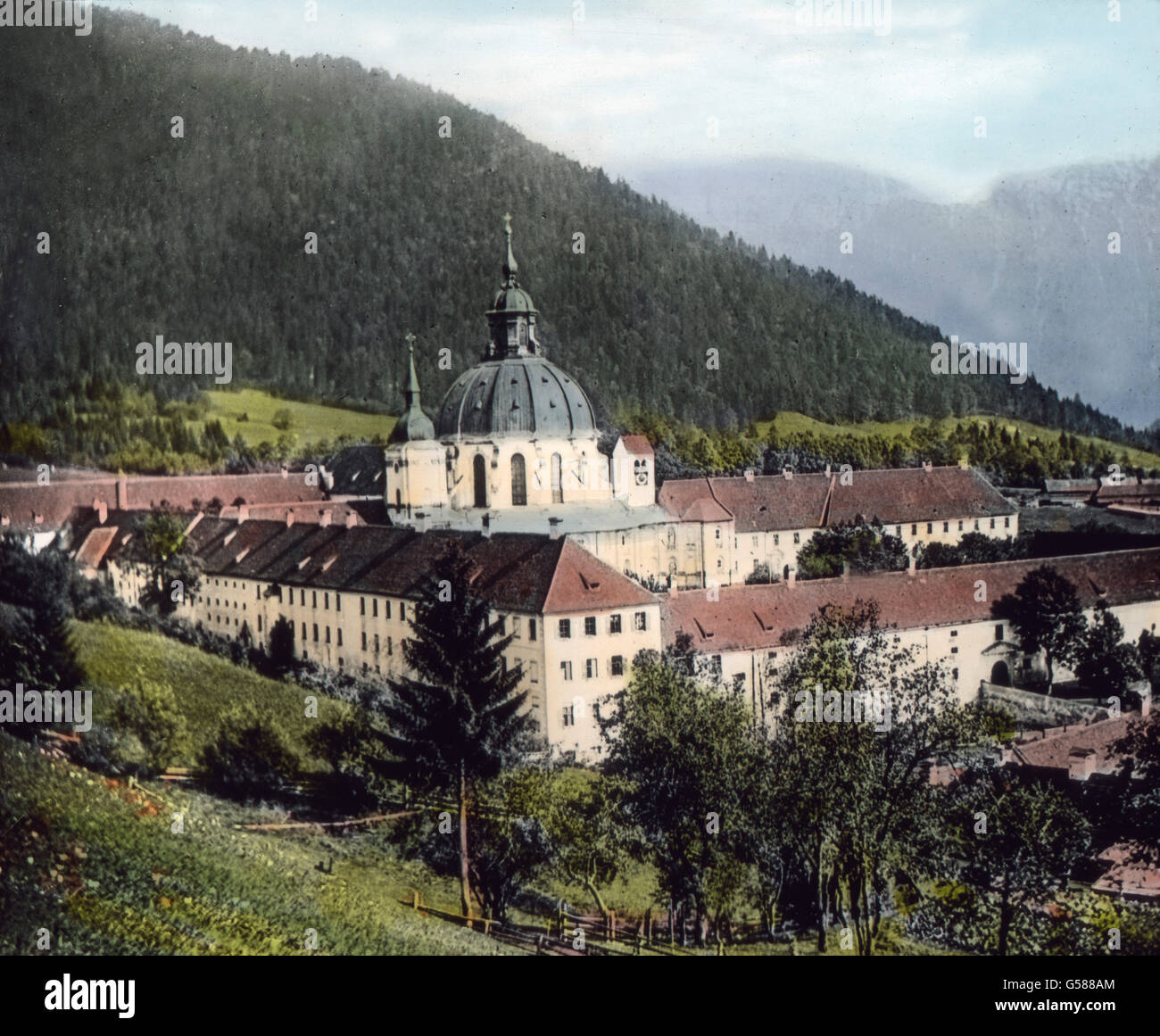 Die Straße, die von Oberau nach Ettal führt, gehört zu den schönsten Bergstraßen Bayerns. In großartigen Kehren windet sie sich den Berg hinauf, an tiefen Schluchten, steilen Abgründen vorbei. Wir haben die Höhe erreicht und zu unseren Füßen liegt in malerischer Ruhe  ringsum von Bergen umgeben das weltberühmte Kloster Ettal. Von weitem grüßt die herrliche Kuppel der Kirche. Kaiser Ludwig der Bayer ist der Erbauer der ursprünglichen Gnadenkirche, von der fast nichts mehr übrig geblieben ist als das Fundament und die Hauptmauern. In der Mitte des 18. Jahrhunderts entstand eine neue Kunstschöpfu Stock Photo