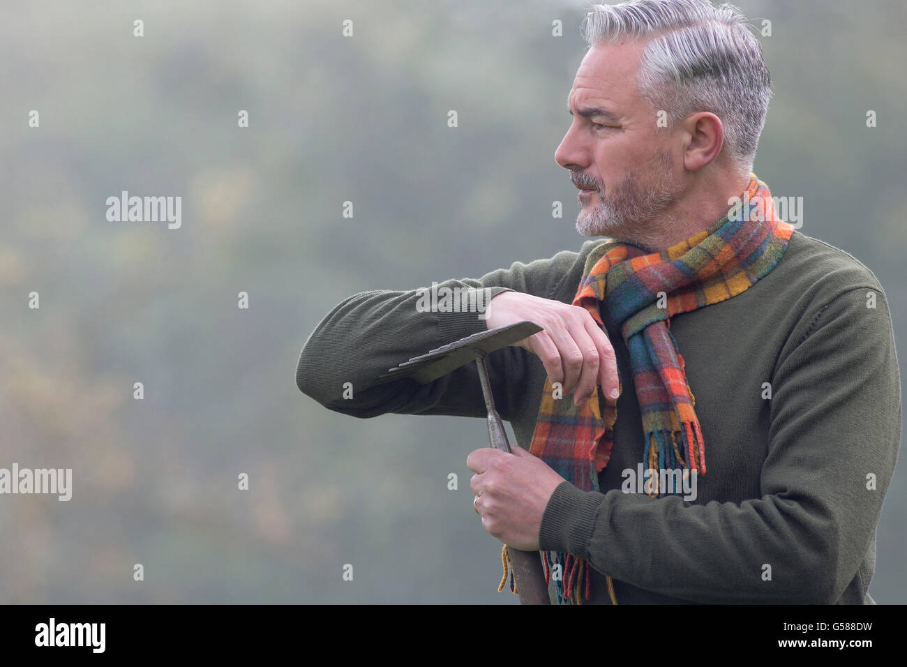Man with a rake looking into the fog on a field. Stock Photo