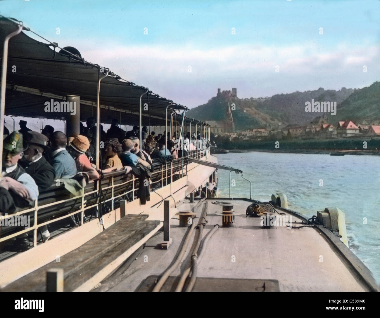 Der Rheindampfer nähert sich dem schönen Rheinstädtchen Oberwesel. Längst ist man in Stimmung. Alles ist ein Herz und eine Seele, alles singt Mein Herz ist im Rheinland, mein Herz ist nicht hier. Europe, Germany, Rhine, Rhine Valley, Rhineland, travel, 1910s, 1920s, 20th century, archive, Carl Simon, history, historical, hand coloured glass slide, people, ship, trip, tour, vacation, holiday, passengers, traveller, tourists, tourism, river, Rhine Valley, enjoying Stock Photo