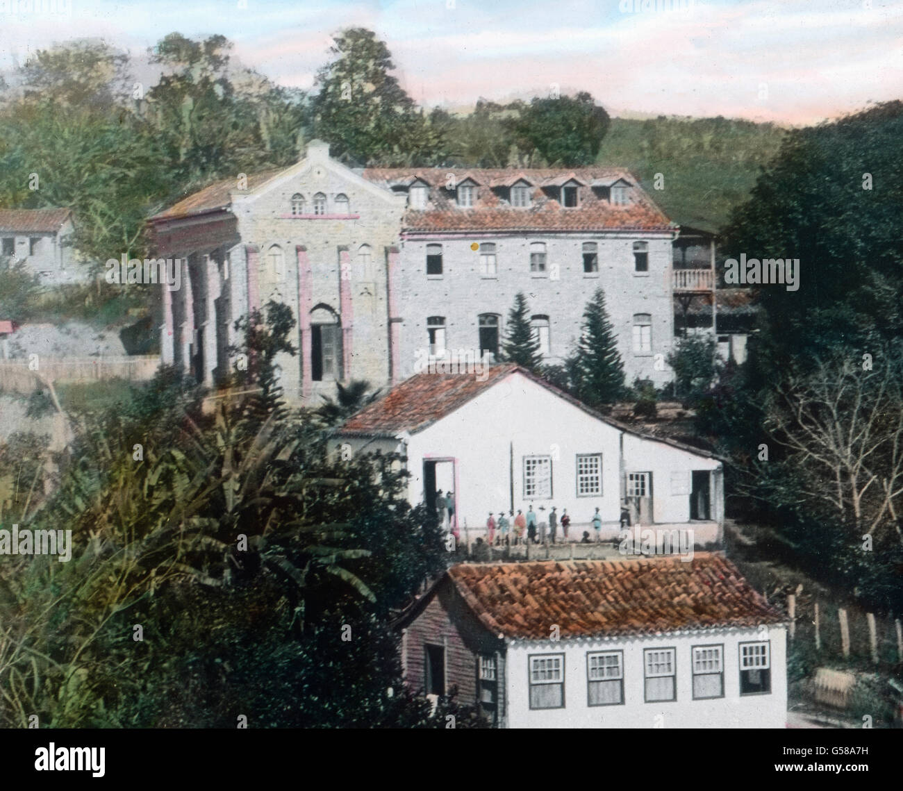 Aus dunklem Walde ragen die weißen Gebäude von Santo Amaro auf, auch einer Siedlung deutschen Ursprungs. Entzückend ist von hier der Blick über Berg und Tal. South America, Brazil, Sant Amaro,  travel, 1910s, 1920s, 20th century, archive, Carl Simon, history, historical, hand coloured glass slide, wood, forest, jungle, houses, civilization, settlement, buildings, architecture Stock Photo