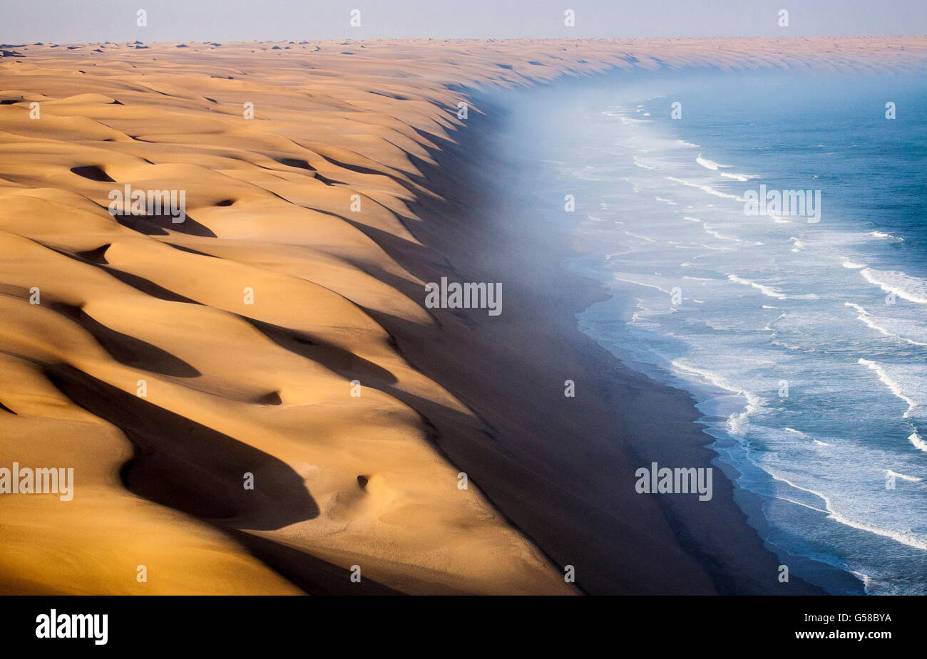The waves of the Atlantic Ocean advance toward the sand dunes of the Namib Desert Namibia Africa Stock Photo