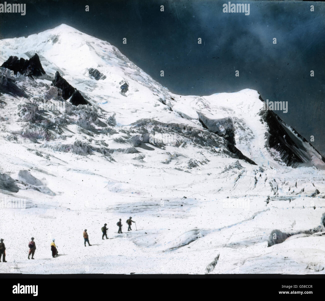 Anfangs geht es nur wenig ansteigend über den Gletscher hinweg, der von zahlreichen Bächlein durchfurcht  und mit Felstrümmern bedeckt ist. An einigen Stellen sammelt sich das Wasser auch in Vertiefungen des Eises an und bilder kleine Teiche, wie einsolcher auf dem Bilde links von den Bergsteigern zu sehen ist, während rechts und nach vorn zu mächtige Spalten sich hinziehen. Sie können hier auch genau den weiteren Anstieg nach dem Grande Mulets verfolgen. Wir müssen das kleine Eistal durchschreiten, daß Sie vor dem furchtbaren Firnbruch der Aiguille du Gouter  (auf der rechten Seiten des Bilde Stock Photo