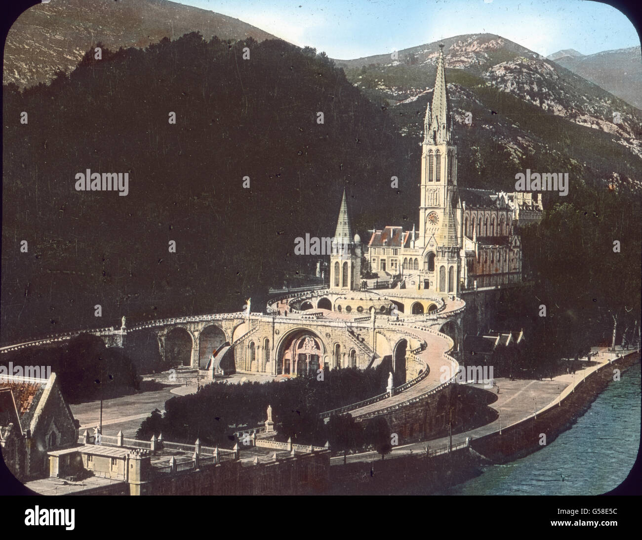 Die Grenze Spaniens und Frankreichs bezeichnet ein himmelhohes Gebirge, die Pyrenäen, das mit all seinen Naturschönheiten noch viel zu wenig bekannt ist und es noch weniger wäre, wenn in ihm nicht der  Wallfahrtsort Lourdes läge, zu dem alljährlich mehr als 100.000 Pilger aus allen Ländern der Erde strömen. Unser Bild zeigt inmitten der gewaltigen Berglandschaft die herrliche Wallfahrtskirche am Ufer der rauschenden Gave de Pau. Während wir an die Pyrenäen,  Lourdes und seine Gnadenwunder  denken, braust unser Schiff weiter an Spaniens und Portugals Küsten vorüber und erreicht nach mehrtägiger Stock Photo