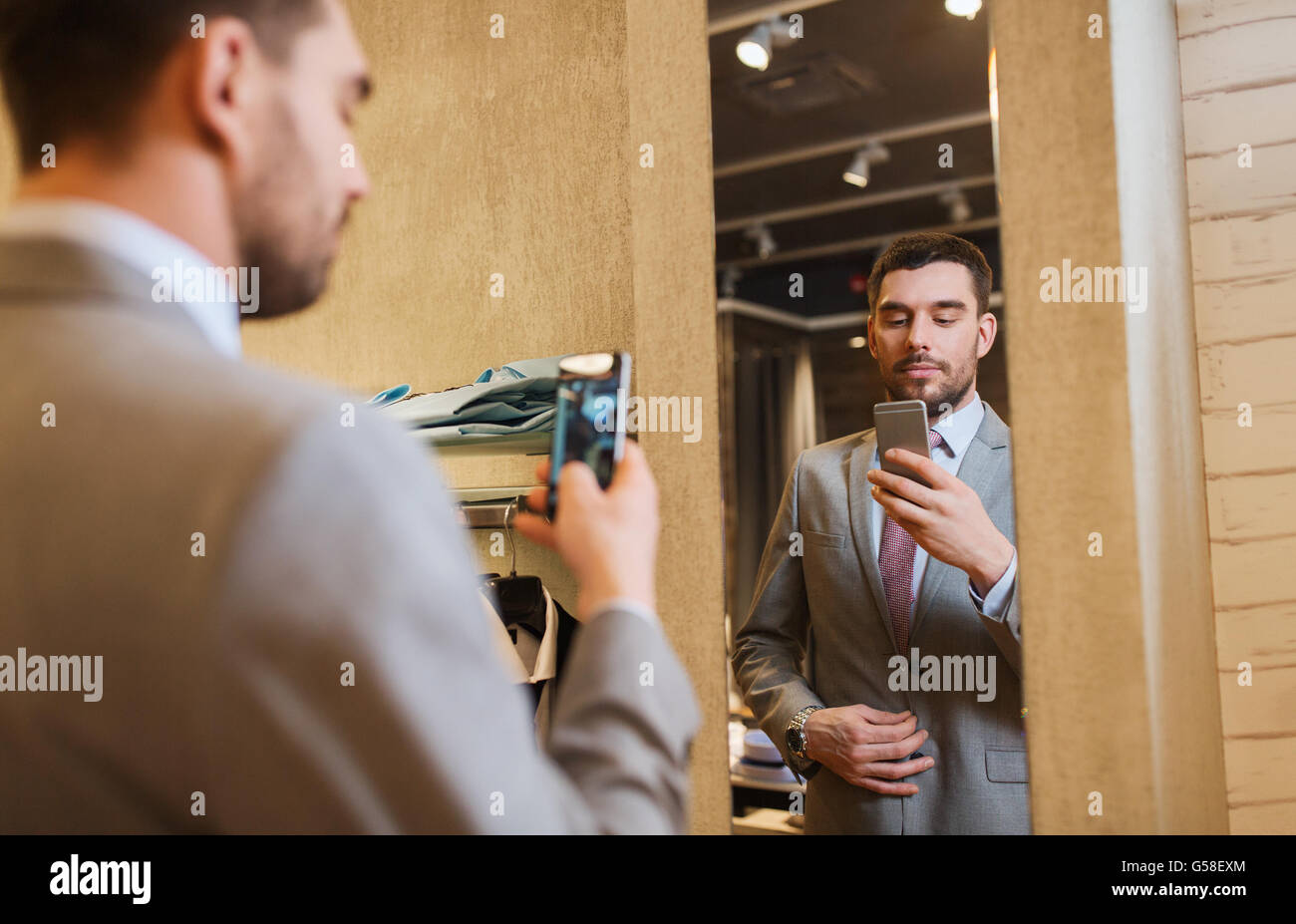 man in suit taking mirror selfie at clothing store Stock Photo