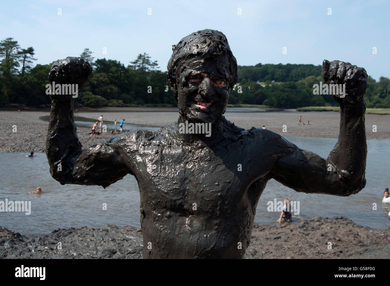 A man covered in mud flexes his muscles by the muddy estuary after swimming in the mud at the Port Eliot Festival Stock Photo