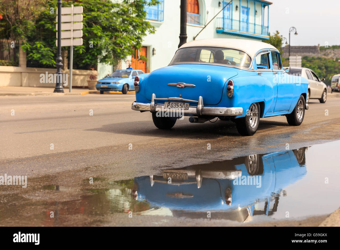 1950s blue Chevrolet American classic car driving,and reflection in a puddle, Havana,Cuba Stock Photo