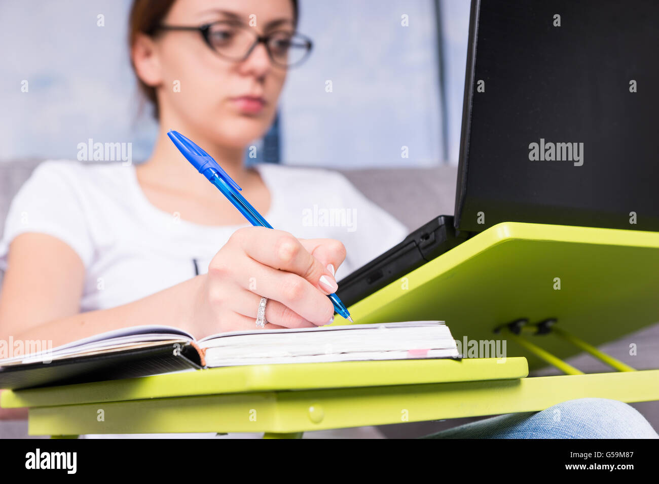 Close up of hand of a young woman who working on a laptop doing her business from home holding a pen as she reads information on the screen. Stock Photo