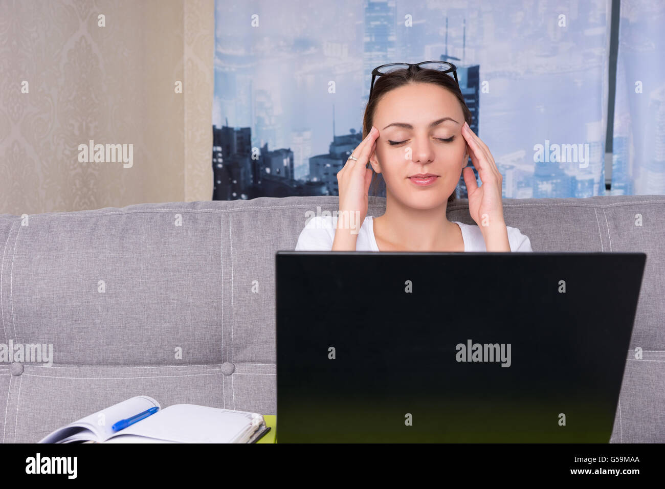 Tired businesswoman making a head massage while working on a laptop and doing her business from home sitting on a sofa Stock Photo