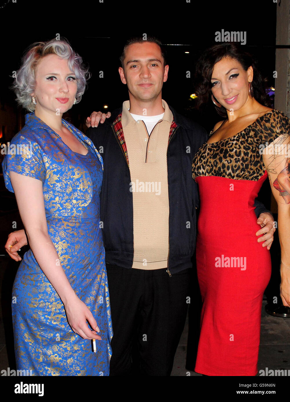 Reg Traviss poses with two burlesque dancers at the opening of Rattlesnake Bar, Islington, London. Stock Photo