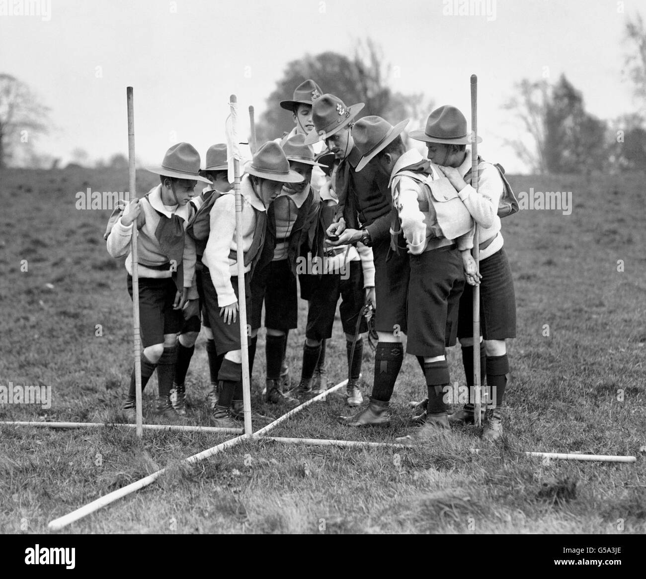 1910: A group of Boy Scouts listen intently to their Scout leader as he instructs them in the art of taking a compass bearing. Stock Photo