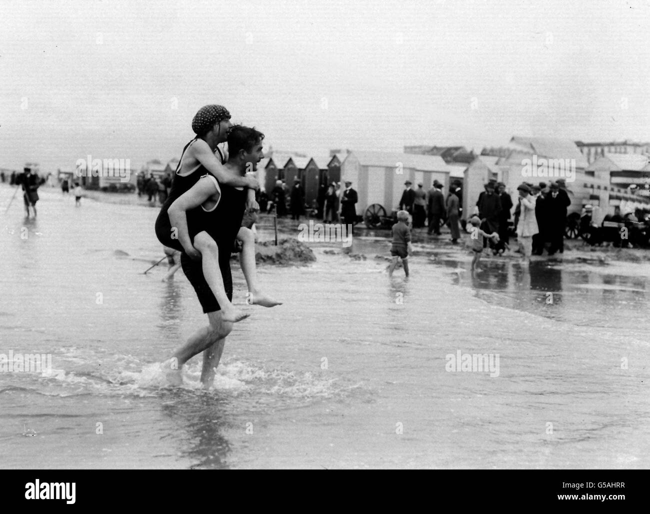 SEA BATHING: A man gives a woman a piggy back as they paddle through the water at a Belgian seaside resort. c1914. Stock Photo