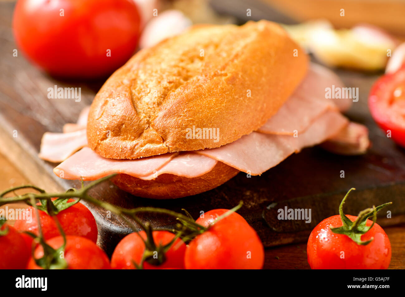 closeup of a braised turkey ham sandwich on a rustic wooden table next to some fresh tomatoes Stock Photo