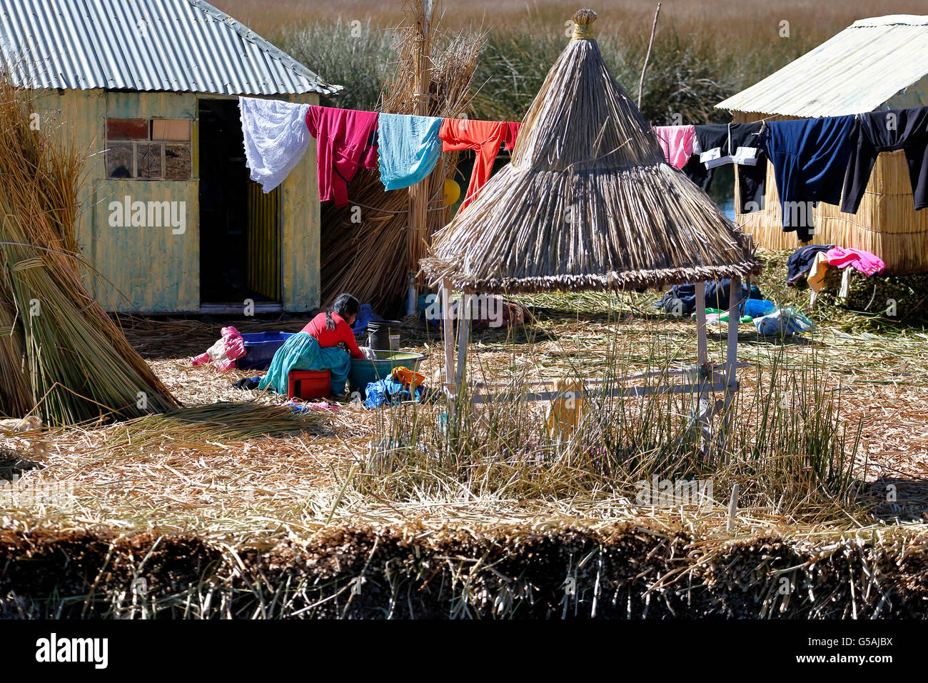 Uros woman, drying laundry and houses on totora reed island, Uros Islands, Lake Titicaca, Puno, Peru Stock Photo