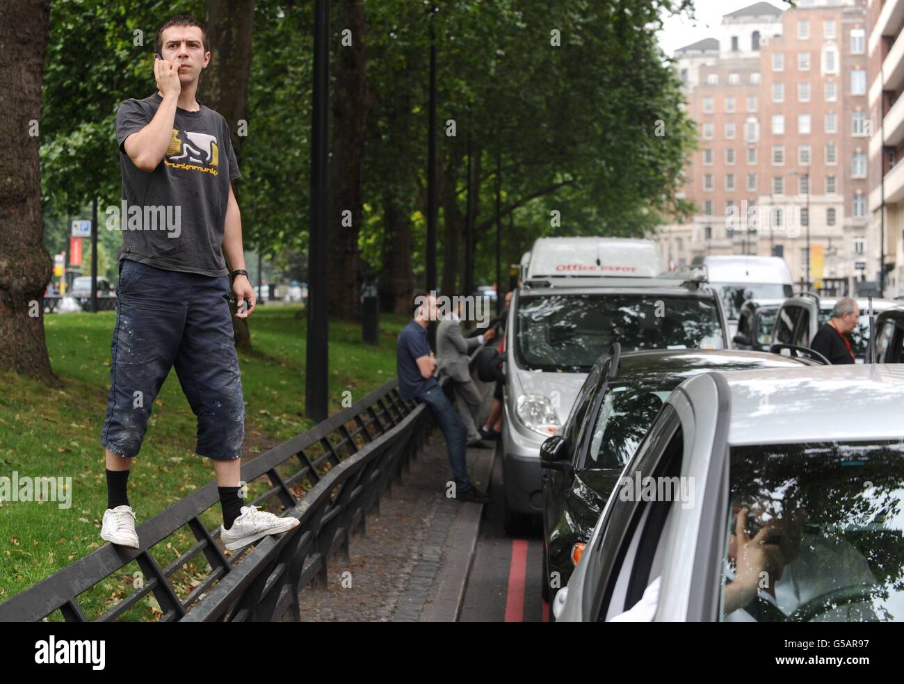 A driver climbs on a roadside barrier beside stationary cars in a traffic jam on Park Lane in central London, as London taxi drivers protested over a ban on using Olympic traffic lanes. Stock Photo