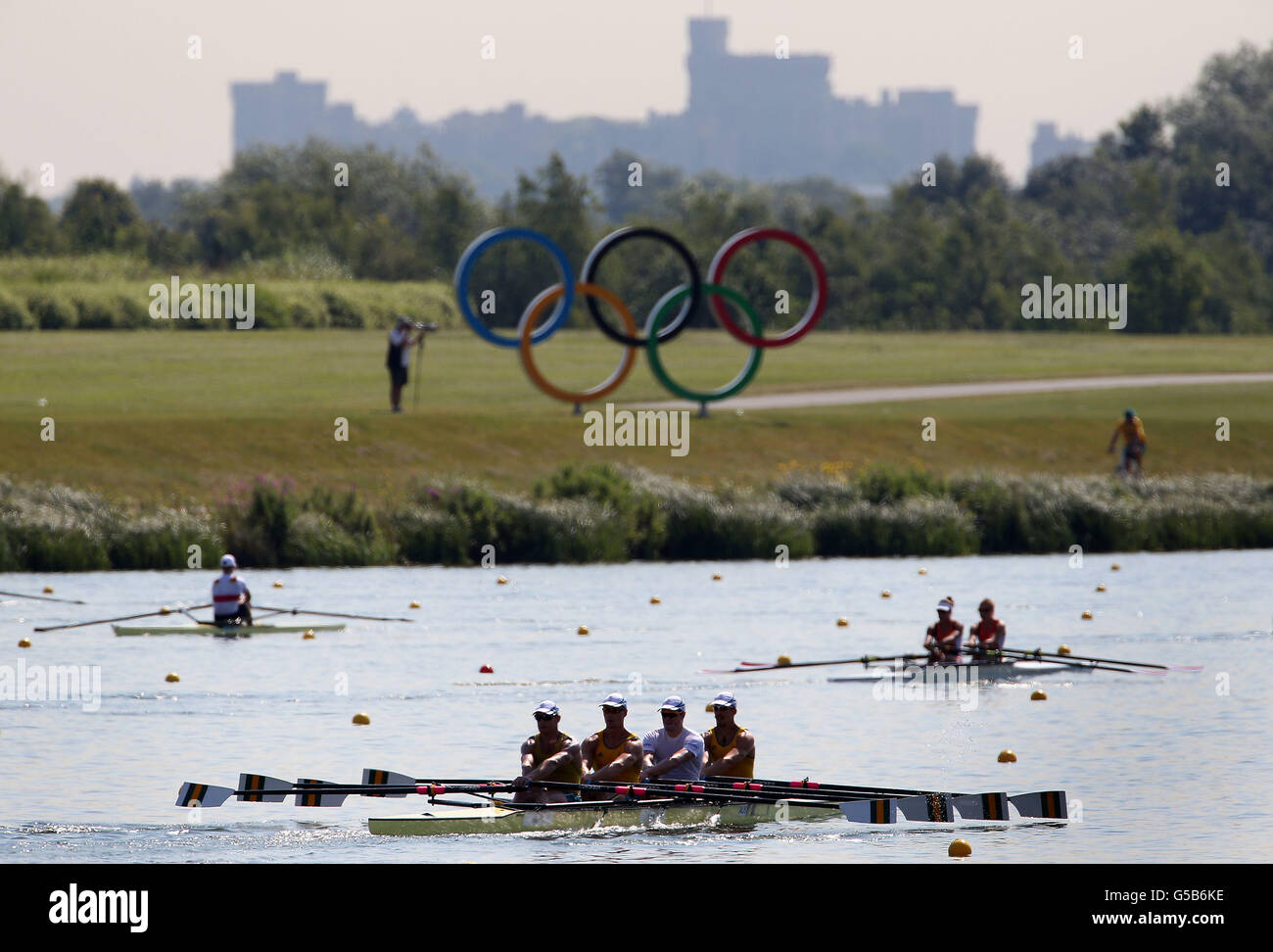 Crews make their way down the course past the Olympic rings and Windsor Castle during the training session at Eton Dorney Rowing Lake, Buckinghamshire. Stock Photo