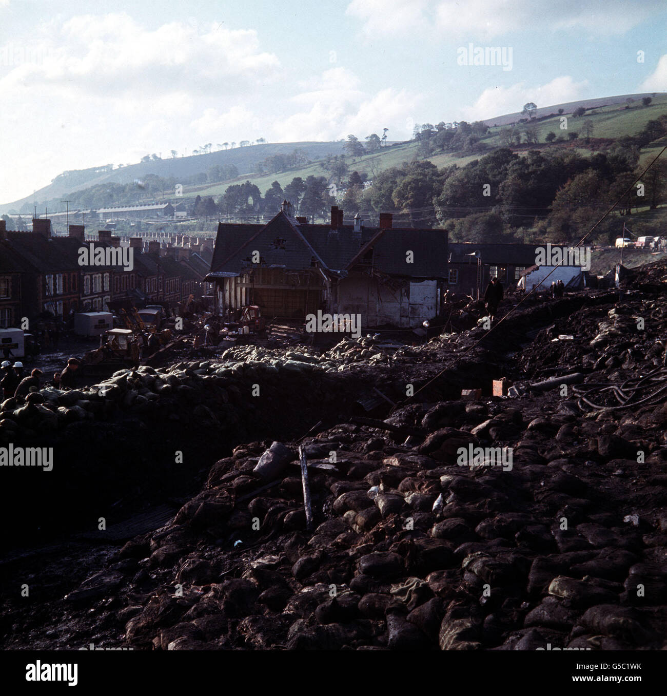 ABERFAN 1966: The mountain that moved. The mass of coal sludge after it moved down and buried 116 children and 28 adults at the Pantglas Junior School (background) at the mining village of Aberfan in South Wales. Stock Photo