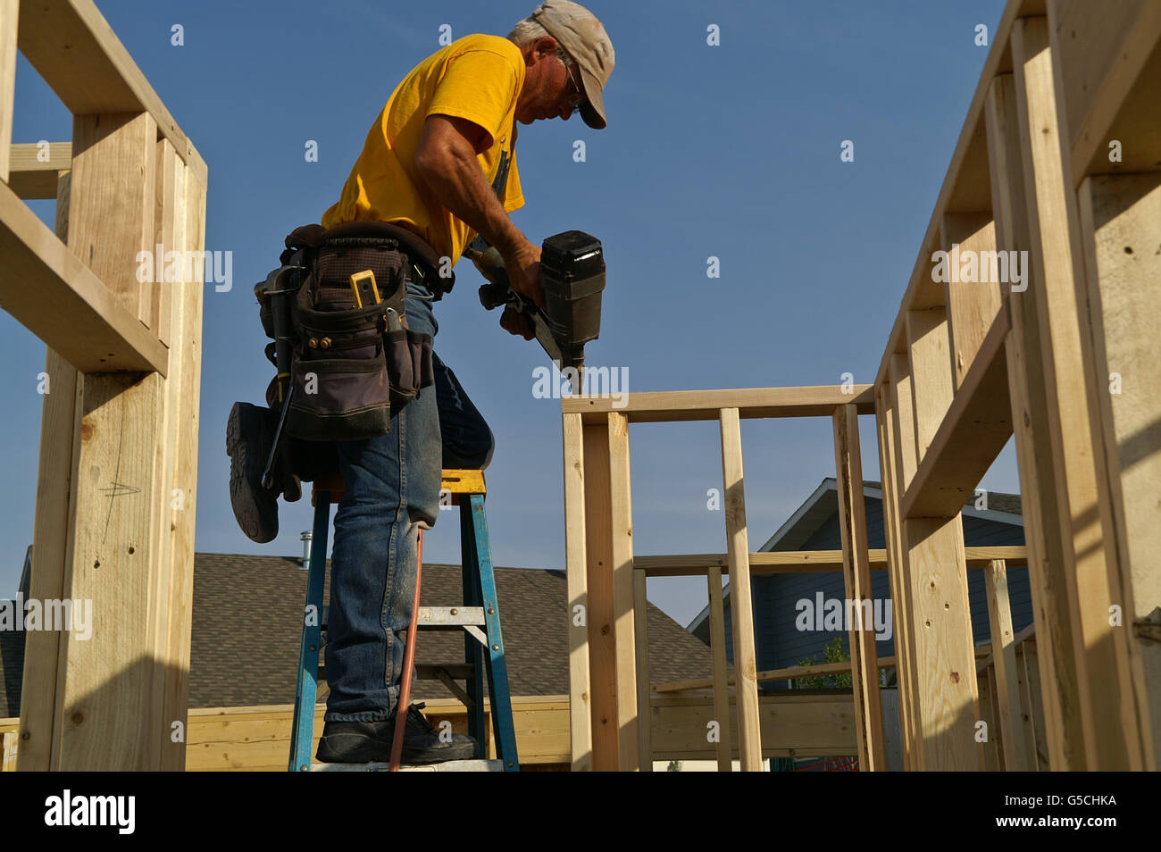 Construction worker standing on a ladder using a nail gun to nail the