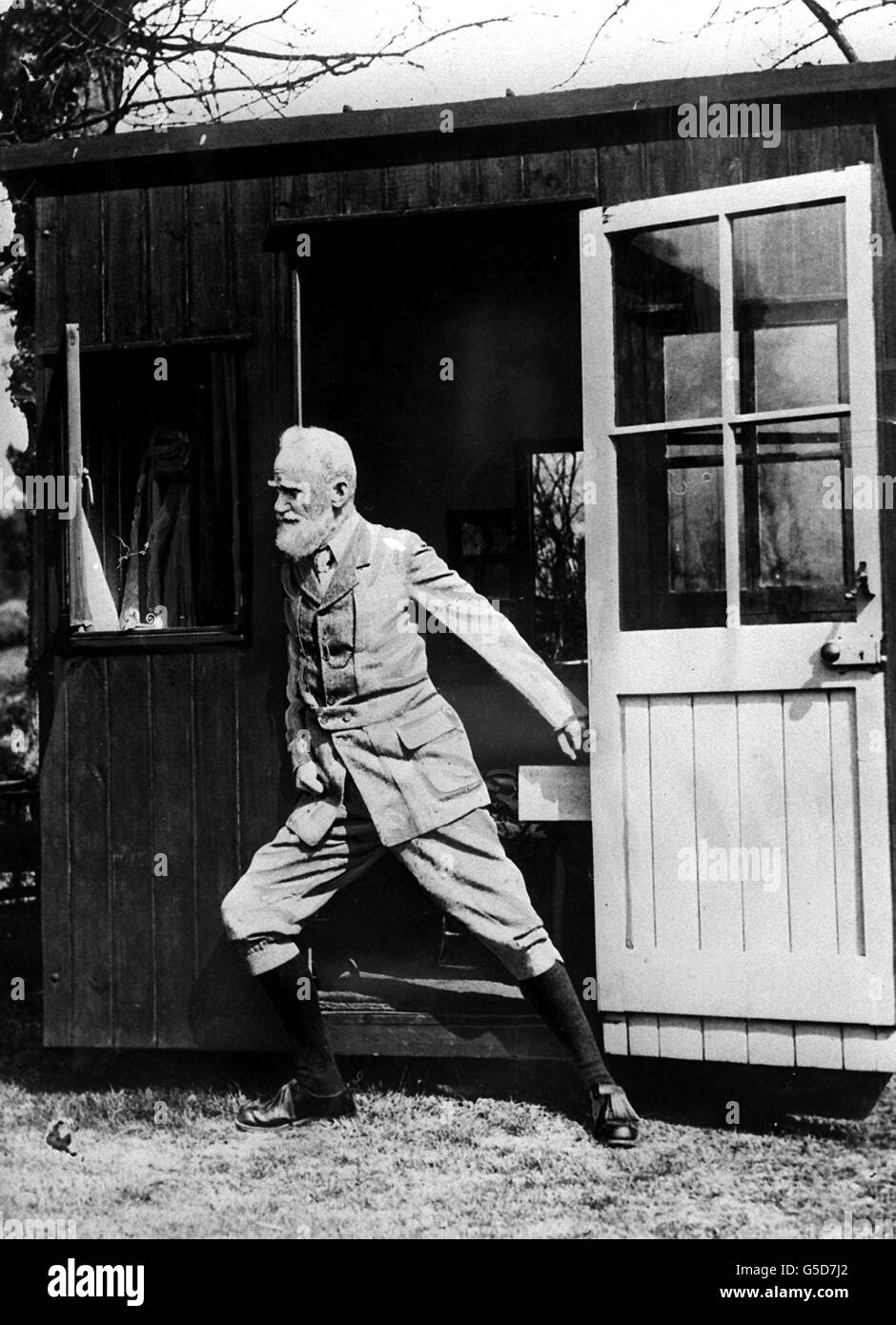 GEORGE BERNARD SHAW 1929: Shaw pushing his revolving sun-hut round to catch the sun's rays. The hut could be manipulated so that on sunny days Shaw could reap the benefit of sun all day. The hut is at Ayot St. Lawrence. Stock Photo
