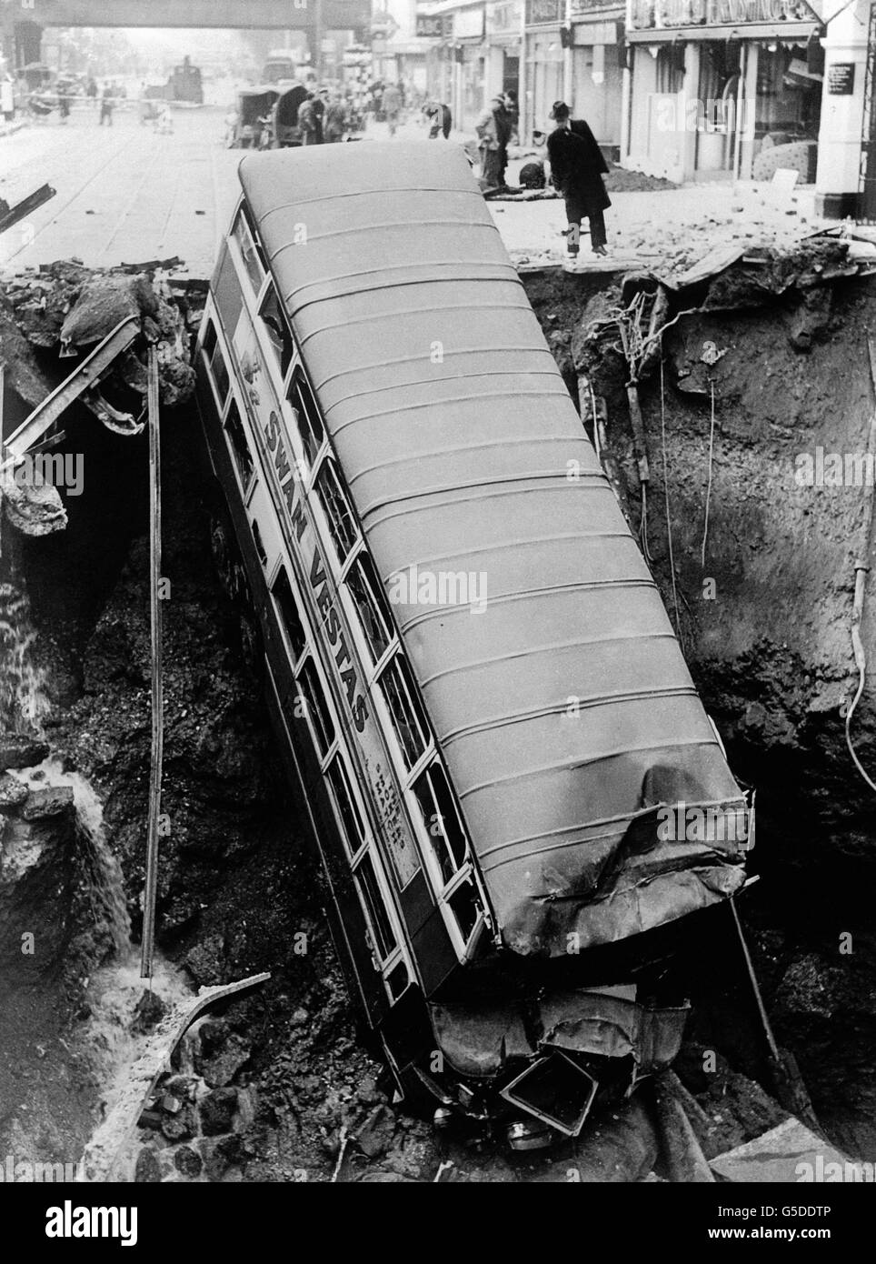 A bus lies in a crater in Balham, south London, following a night-time bomb blast during the blitz. Stock Photo
