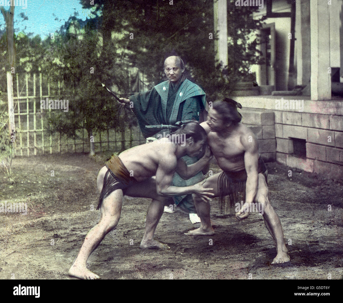 Zwei Sumo-Ringer beim Ringkampf und ihr Schiedsrichter.  Asia, Japan, Asiatic, travel, 1910s, 1920s, 20th century, archive, Carl Simon, history, historical, Japanese, fight, fighter referee, Sumo, wrestling, wrestler, training, fighting, hand coloured glass slide Stock Photo