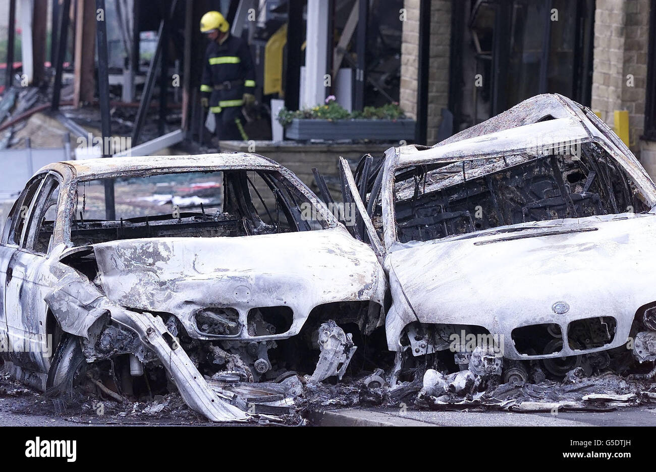 A firefighter leaves the remains of a BMW showroom in Bradford which was burned out and over 14 brand new BMW cars torched, during violence in the town. Stock Photo