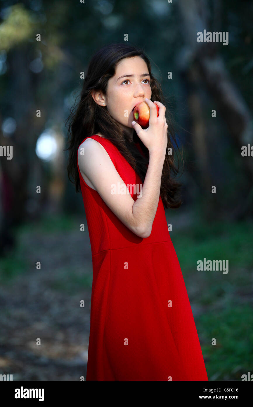 Young girl in red dress eats an apple outdoors Stock Photo