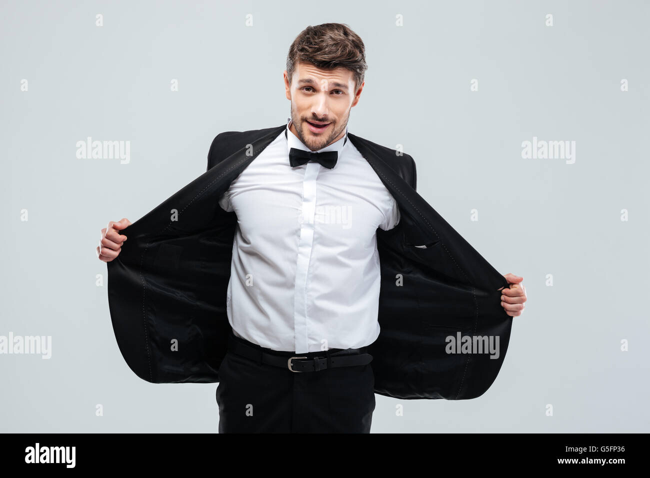 Smiling young man in tuxedo with bow tie taking off his jacket Stock Photo