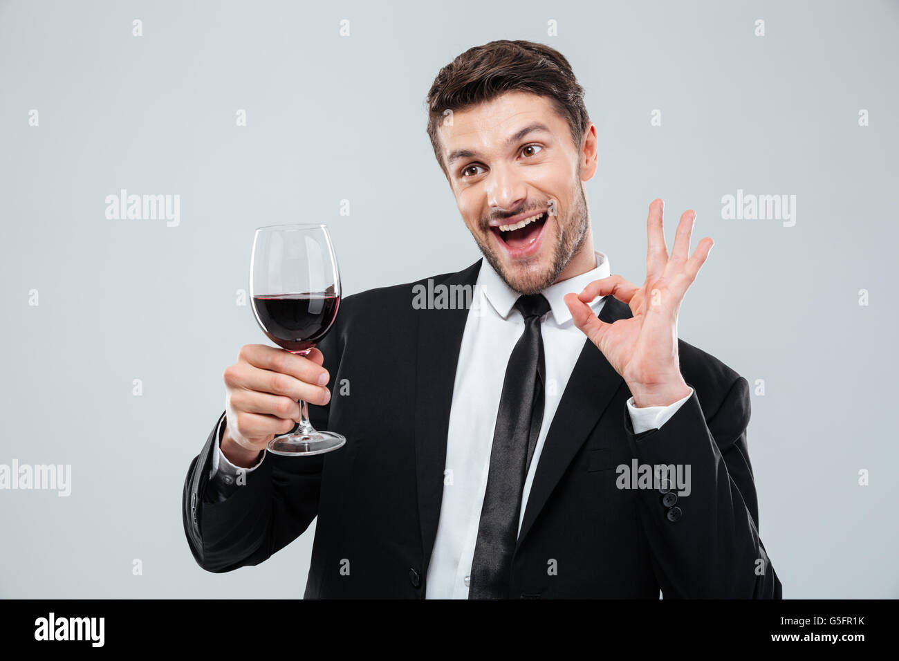 Funny cheerful drunk businessman drinking red wine and showing ok sign over white background Stock Photo