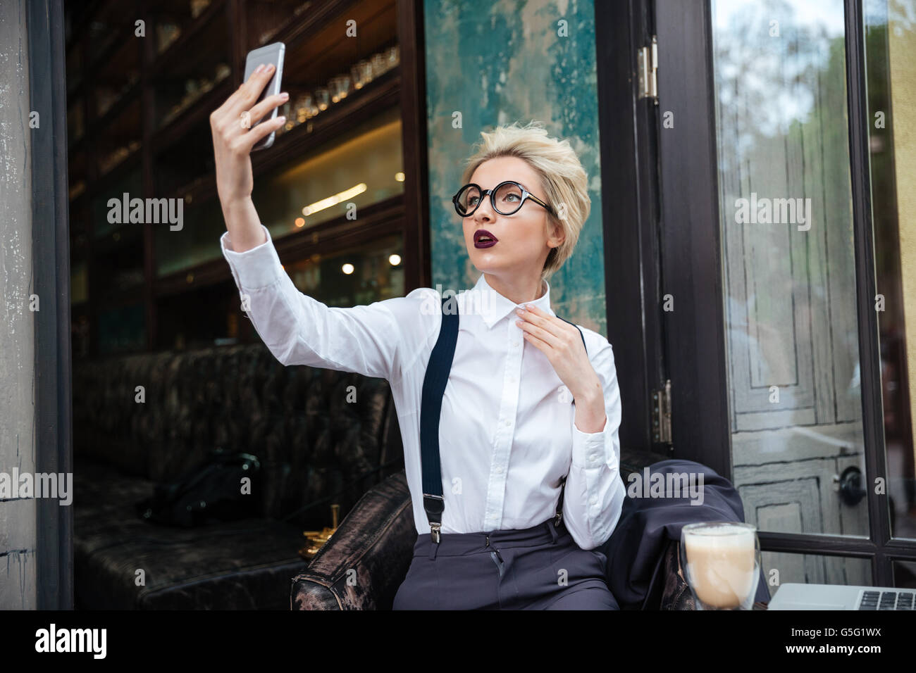 Stylish young woman in round glasses taking selfie in cafe Stock Photo ...