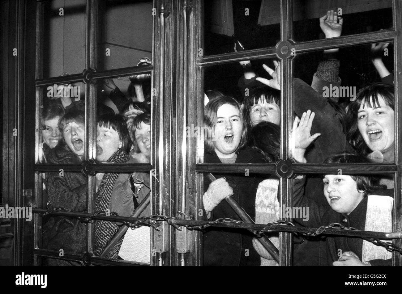 Screaming fans outside the heavily-chained doors of the Scala Theatre, London. Inside were the Beatles, shooting scenes for their first film. Police guarded the doors although some teenagers were allowed in to play the role of extras in the film. Stock Photo