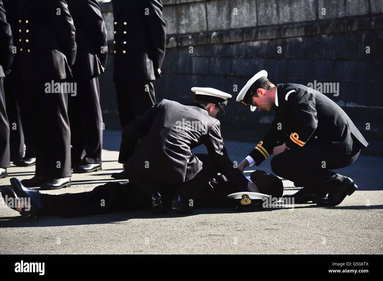 Naval officers attend to another officer who collapsed during a passing out parade at the Britannia Royal Naval College in Dartmouth where Prime Minister David Cameron took the salute. Stock Photo