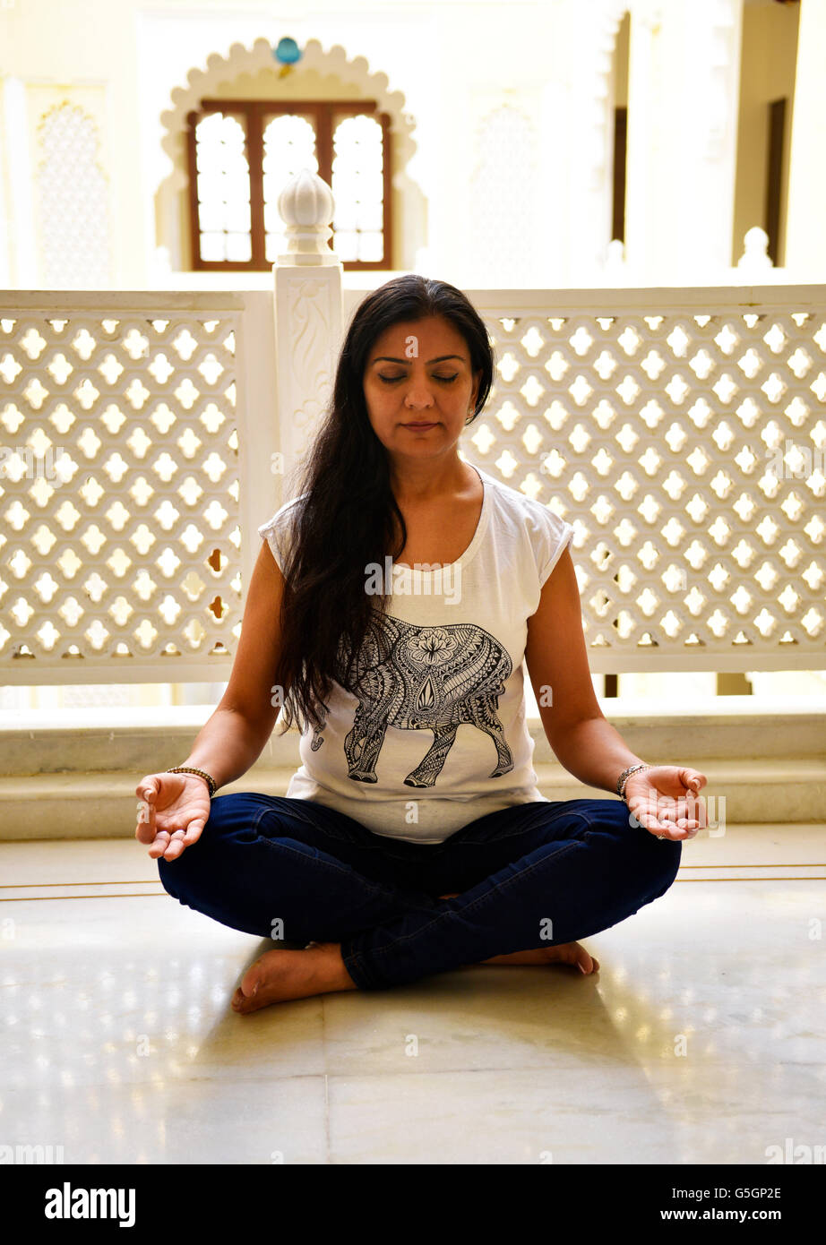 Beautiful woman with luscious locks seated cross legged on floor in intense meditation connected into deep spiritual experience. Stock Photo