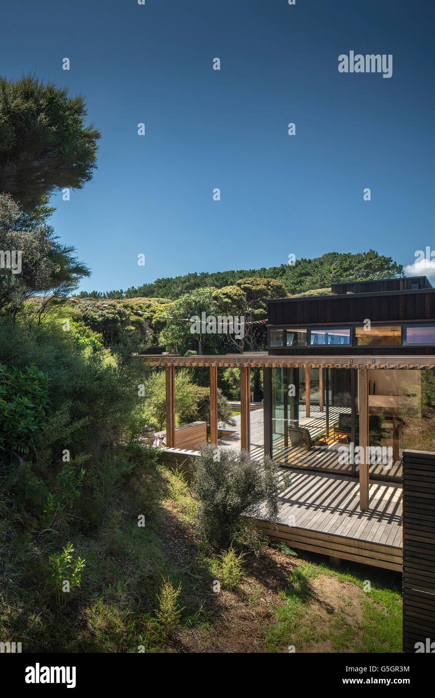 Side of house with wooden sun slats and decking and surrounding bush / countryside. Blue sky and sun. PEKA PEKA II HOUSE, Peka Peka - Kapiti Coast, New Zealand. Architect: HMA, 2016. Stock Photo