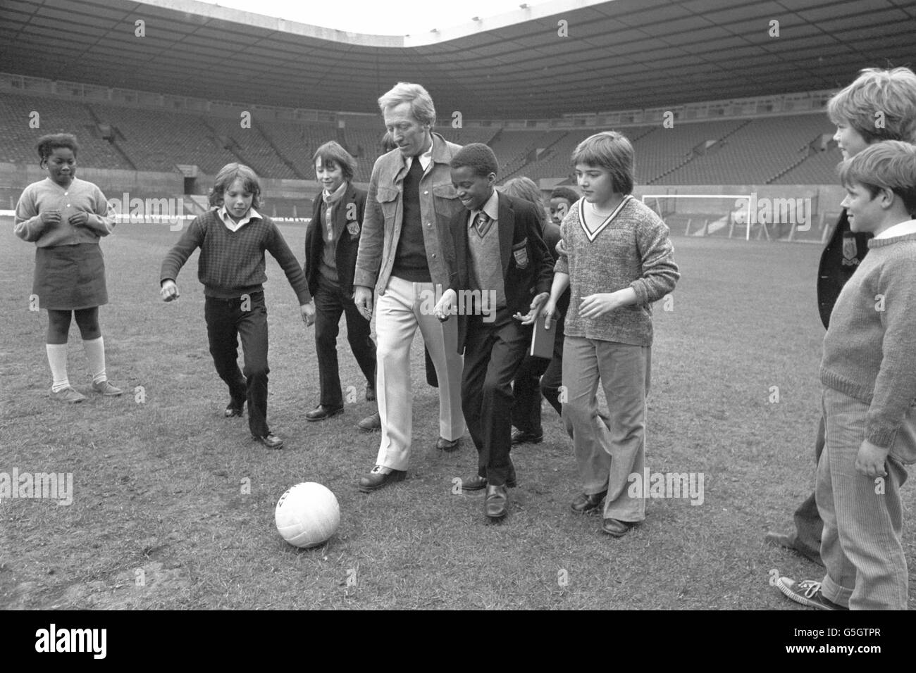 American singer Andy Williams is given a football lesson by local children during a visit to Manchester United's Old Trafford football ground. Stock Photo
