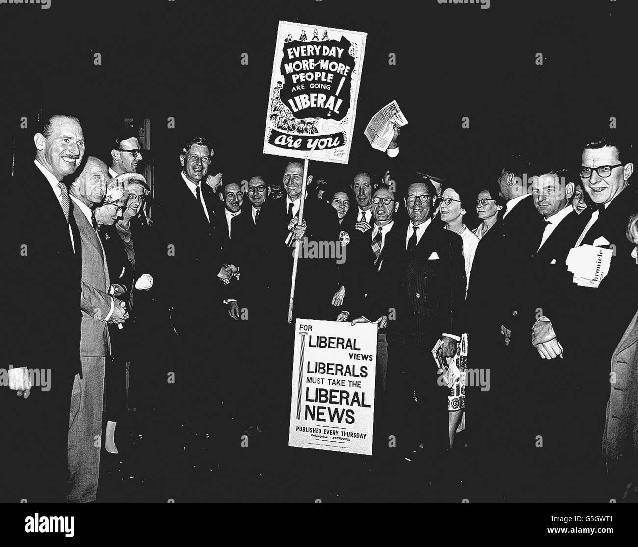 The leader of the Liberal Party, Mr. Jo Grimond, is greeted by Mr. David Brooke (shaking hands and holding placard) and other Liberals, notably Mr. Robin Day ( far right), on Mr. Grimond's arrival at King's Cross station, London, from Aberdeen. Mr. Grimond has left his constituency, Orkney and Shetland, to open the Liberals' general election campaign with a meeting at the Central Hall, Westminister, London. Stock Photo