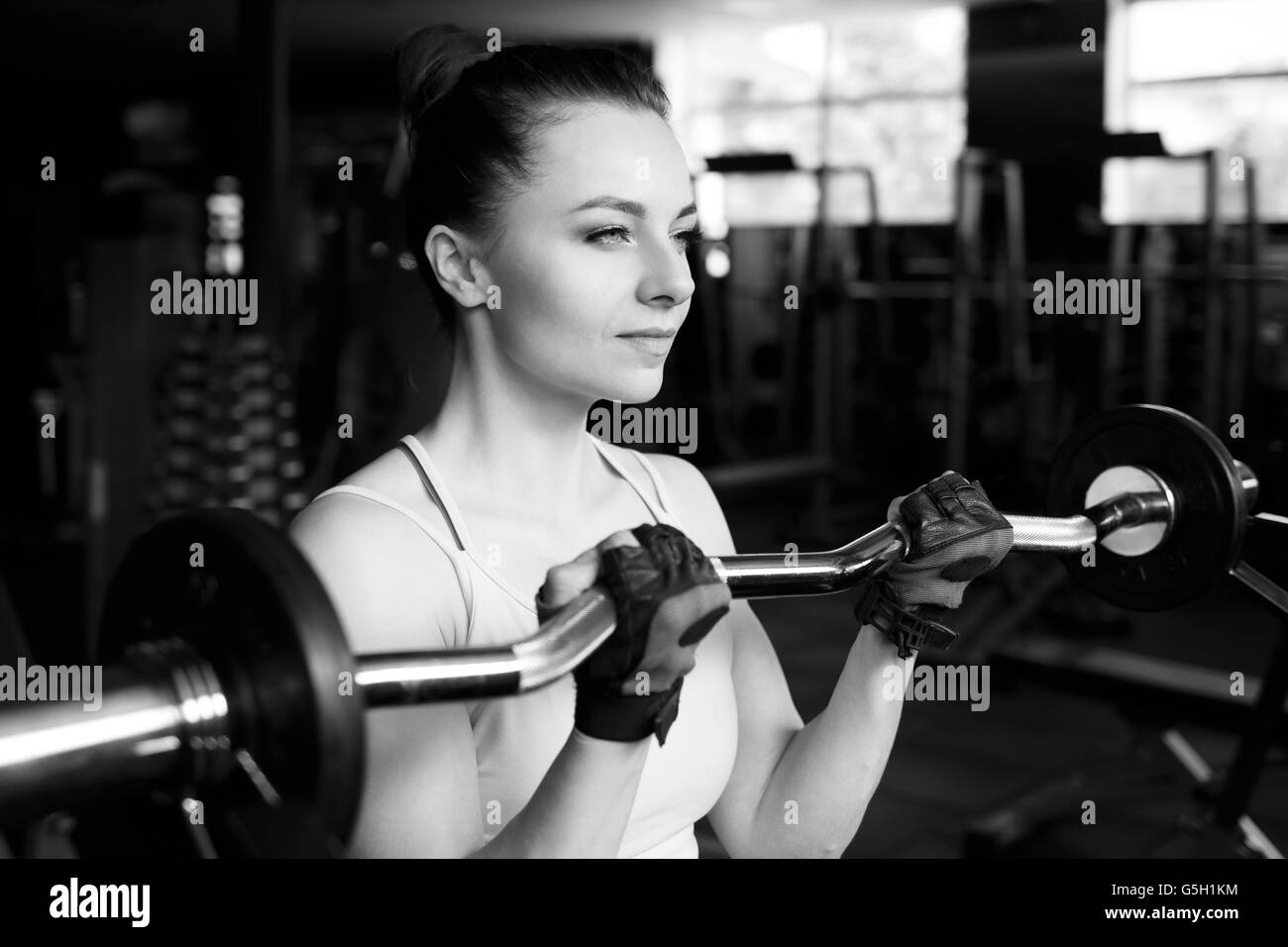 Young beautiful woman doing biceps curl with EZ curl bar in a gym. Athletic girl doing workout in a fitness center Stock Photo