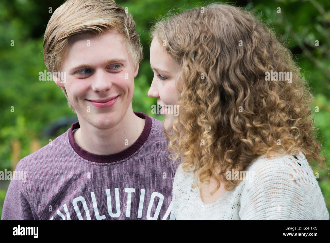 Happy teenage couple chatting outside, he is smiling at her while she