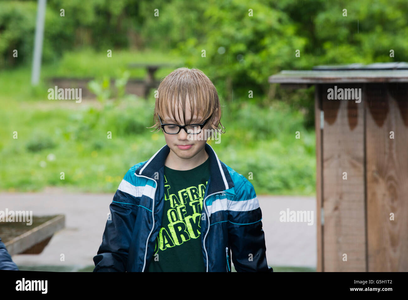 Portrait of a young boy with rain coat and wet hair outside wearing glasses. Stock Photo